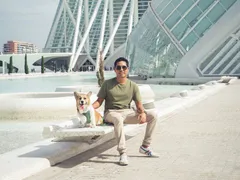 Emilio wearing sunglasses on a sunny day, sitting in front of a building with his dog